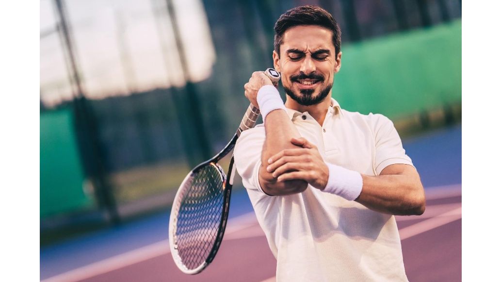 man with tennis racket holding elbow in pain